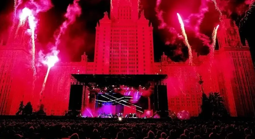 Ogromny budynek oświetlony na czerwono, fajerwerki i scena koncertowa. Tłum ludzi czeka na największy koncert na świecie.