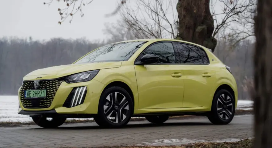 Żółty Peugeot e-208 stoi na tle drzew i zimowego krajobrazu.