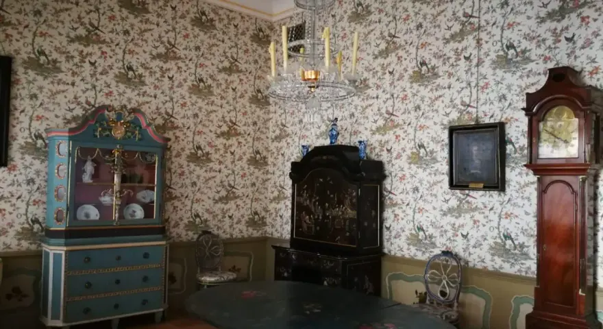 Wnętrze Uphagen House: zabytkowy zegar, szafka, stół i tapeta z ptakami.
