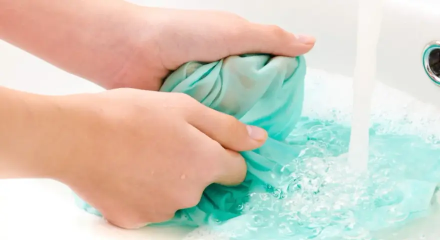 Hände waschen ein türkises Tuch im Waschbecken, um Fettflecken zu entfernen. Wasser sprudelt und schäumt.