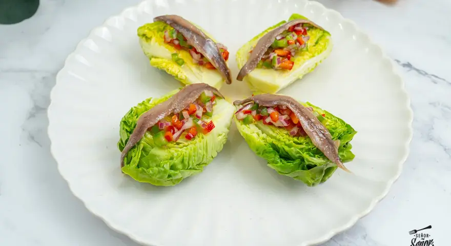 Cuatro cogollos de Tudela rellenos de pimientos y cebolla, coronados con anchoas. Frescura y sabor en cada bocado.