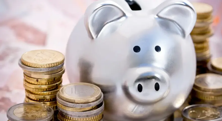 Hucha plateada rodeada de pilas de monedas de euro, simbolizando las ventajas del euro para el ahorro.