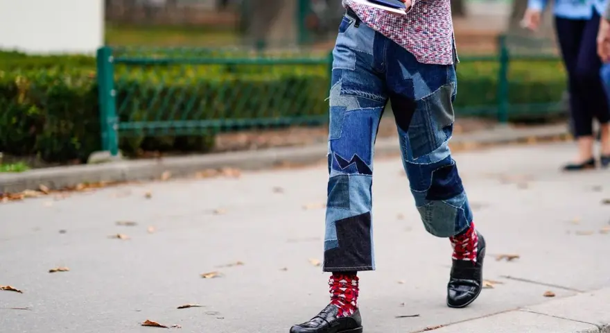 Uomo con jeans patchwork e mocassini neri, calzini rossi a fantasia.