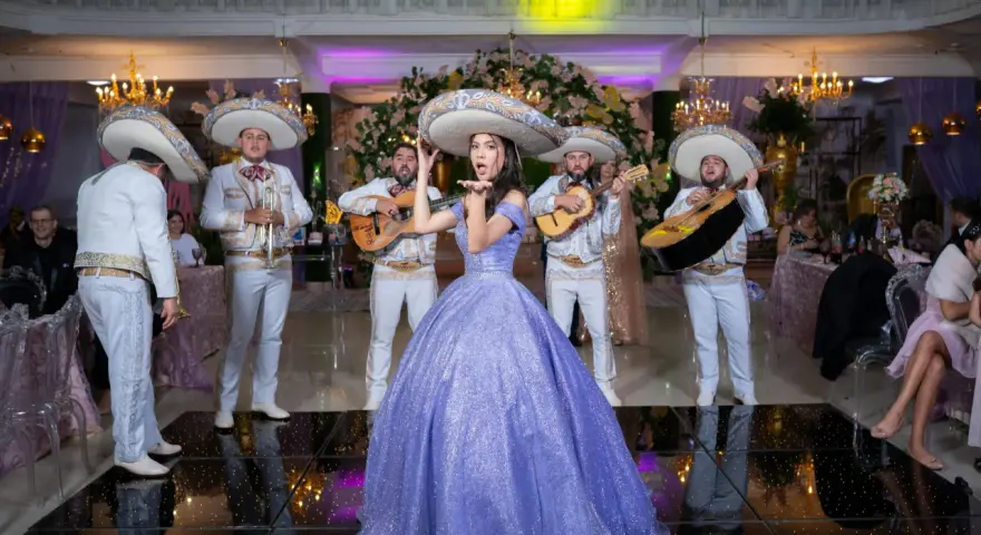 Mariachi grają, a dziewczyna w fioletowej sukni posyła całusy. W tle weselne dekoracje i goście. Idealna sceneria do przyśpiewki weselne tekst.