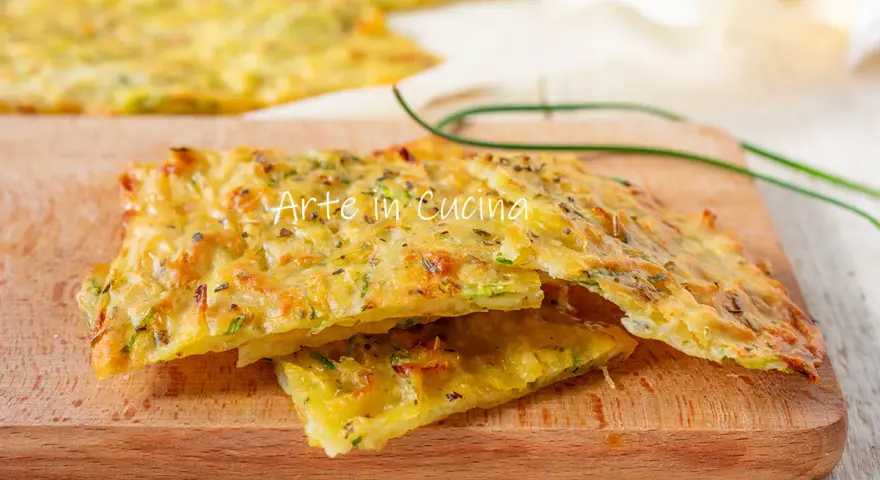 Schiacciata di zucchine dorata e croccante, con erbe aromatiche, servita su un tagliere di legno.