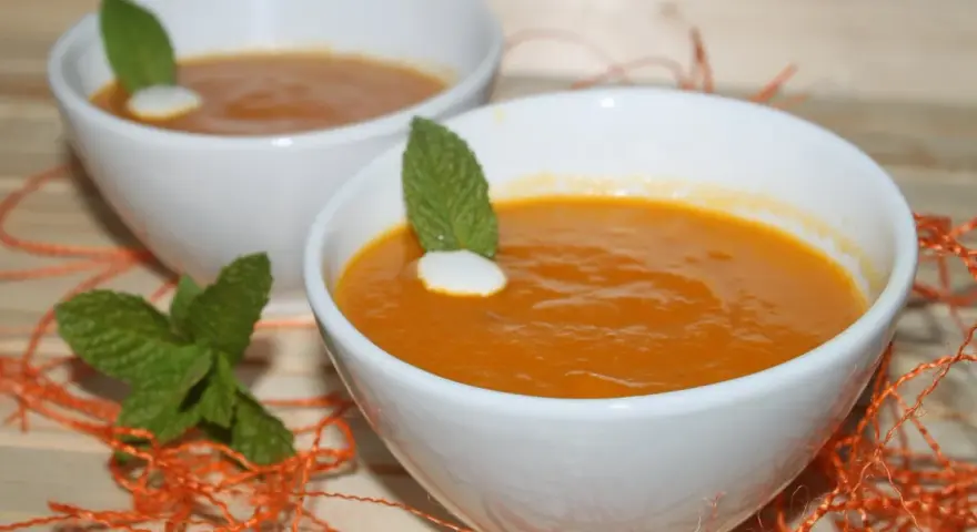 Dos cuencos blancos con crema de calabaza naranja, decorados con menta y un toque de nata.