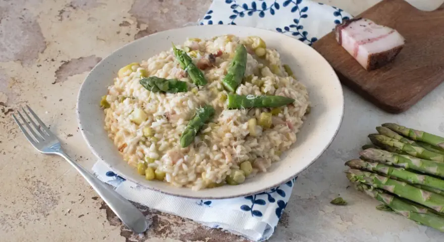 Un cremoso risotto con asparagi e pancetta, guarnito con punte di asparagi freschi e parmigiano.