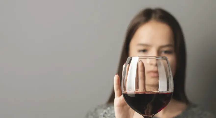 Kobieta odrzuca kieliszek z czerwonym winem, symbolizując walkę z pokusą, która może prowadzić do dawki śmiertelnej alkoholu.
