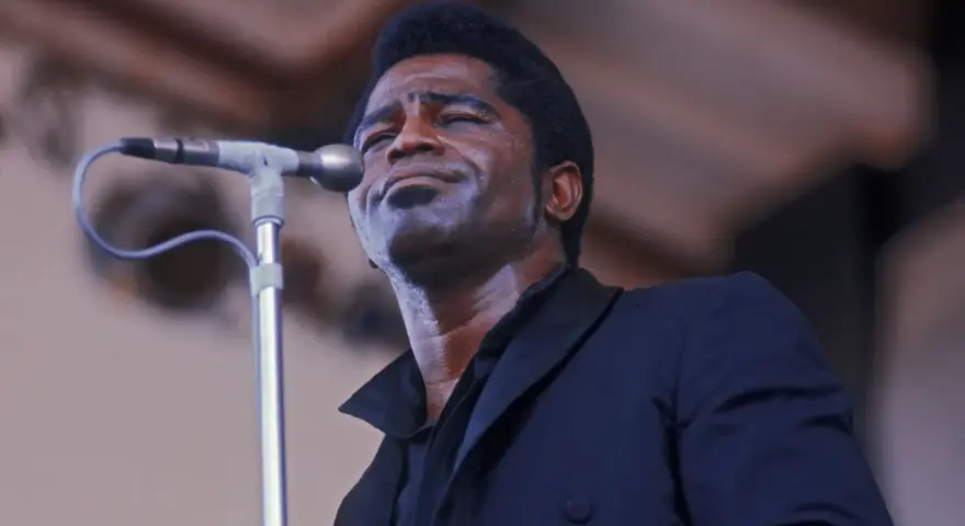 Le chanteur funk français James Brown, en sueur, chante passionnément dans un microphone.