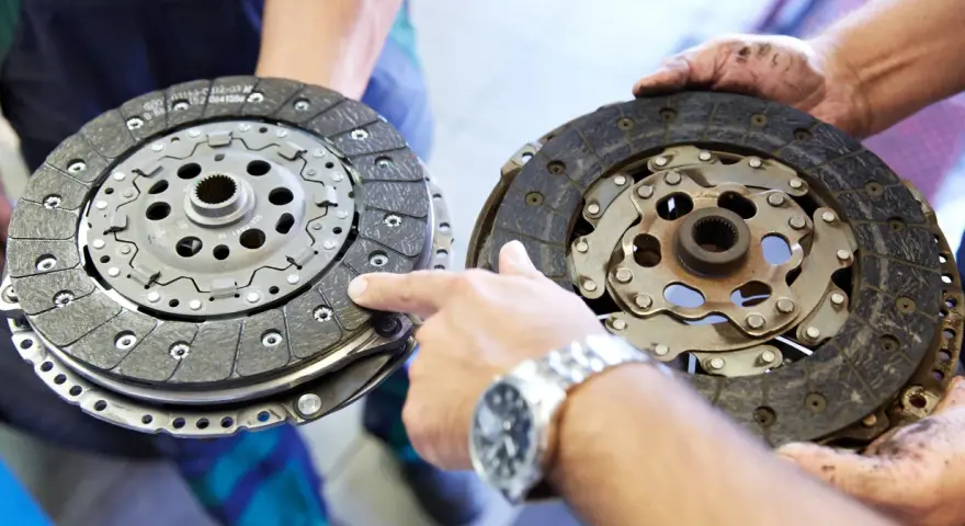 Mechanik pokazuje dwa dyski sprzęgła: jeden nowy, drugi mocno zużyty, z widocznymi śladami spalonego sprzęgła.
