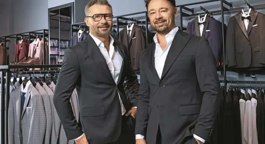 Dwóch eleganckich mężczyzn w garniturach, w sklepie z odzieżą męską. Czy to Pako Lorente czy Vistula?