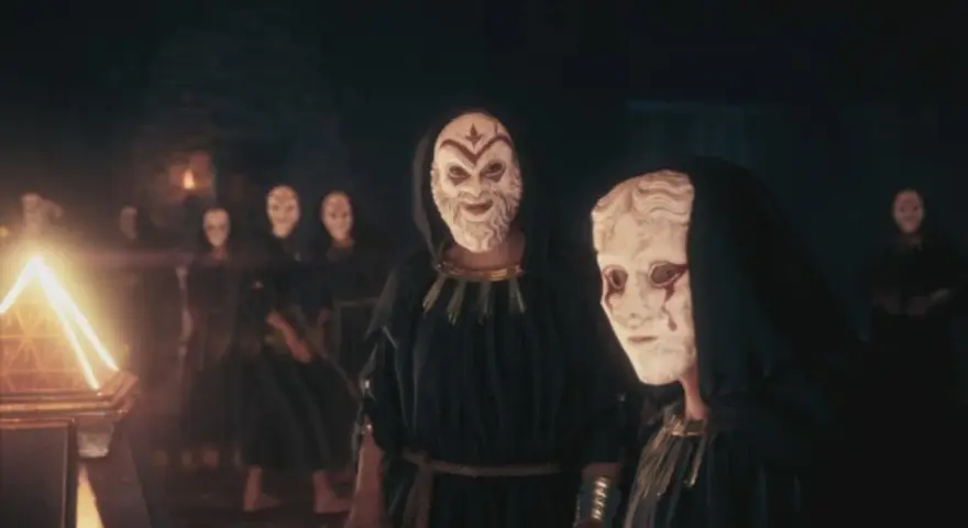 Miembros del culto de Kosmos, con túnicas oscuras y máscaras blancas, se reúnen ante un objeto piramidal brillante.