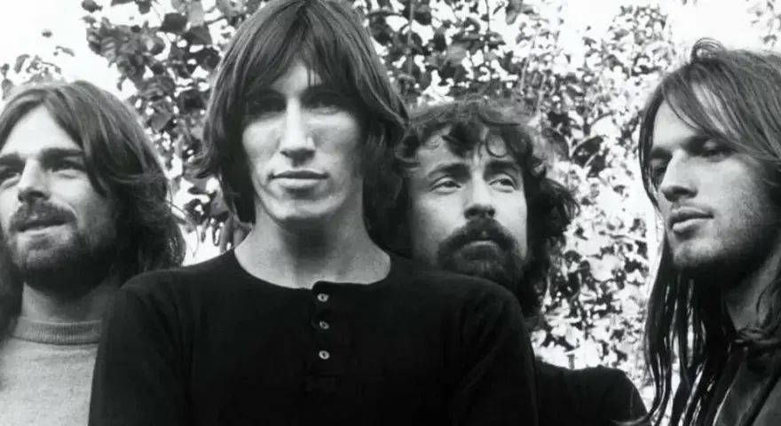 Quatre musiciens aux cheveux longs, dans un style musical Pink Floyd, posent devant un feuillage.