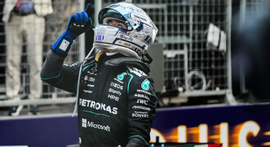 Piloto de F1 con casco y guantes azules levanta el dedo índice, celebrando una victoria en la carrera F1 Mónaco.