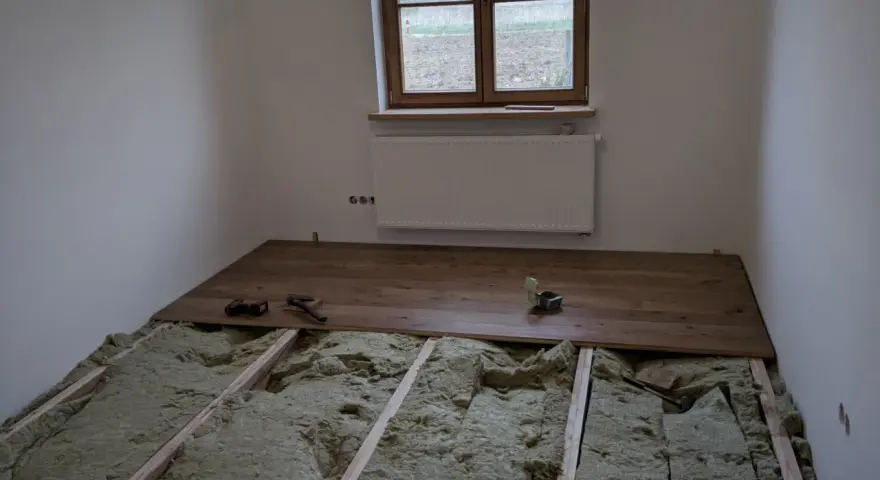 Podłoga na legarach na poddaszu, w trakcie montażu drewnianych desek. Widoczna wełna mineralna izolacyjna.