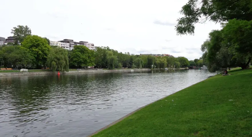 Grüne Ufer am Landwehrkanal Berlin mit Bäumen, Gebäuden und Menschen, die sich auf der Wiese entspannen.