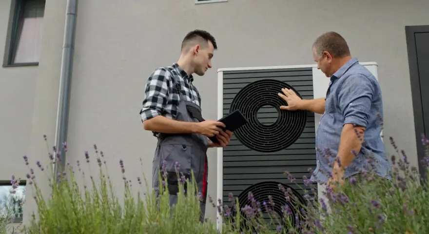 Technik z tabletem i klient przy pompie ciepła. Rozmawiają o ekonomicznym ustawieniu pompy ciepła, by zapewnić optymalne ogrzewanie domu.