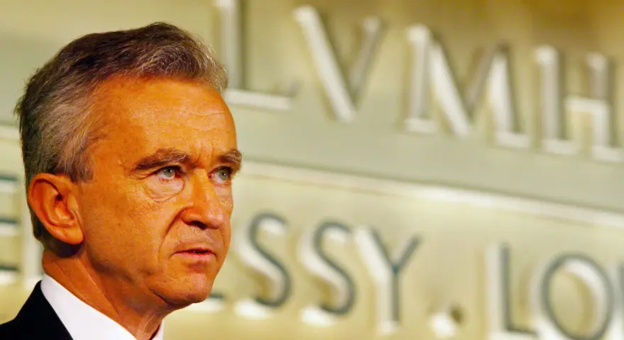 Bernard Arnault, proprietario Dior, guarda pensieroso. Sullo sfondo, il logo LVMH.