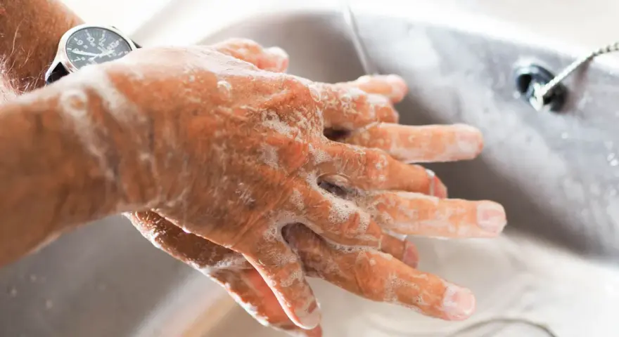 Manos con jabón bajo un chorro de agua en un lavabo.