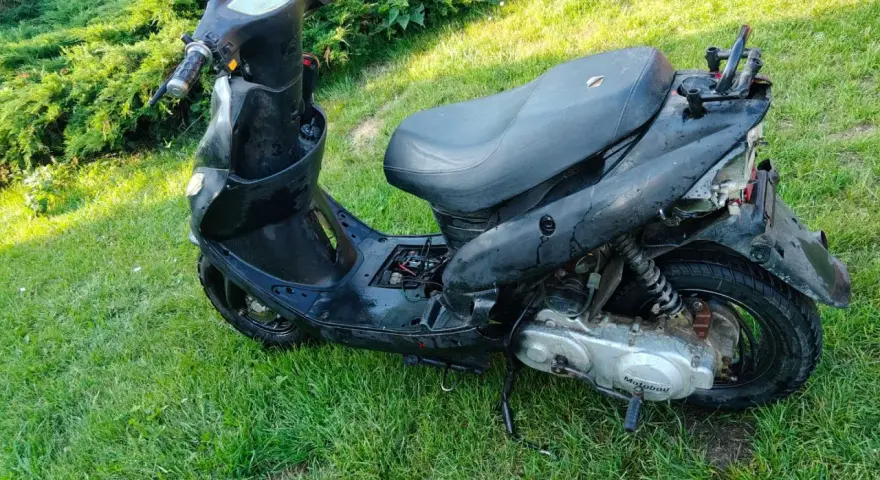 Czarny skuter diesel, nieco zniszczony, stoi na trawie.