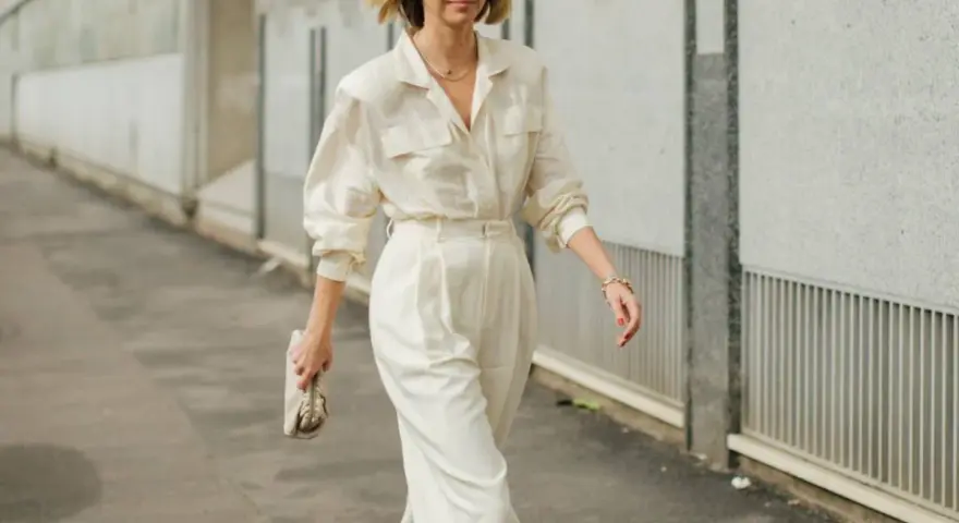 Mujer con un elegante outfit oficina verano: pantalón ancho blanco, camisa holgada y bolso de mano.