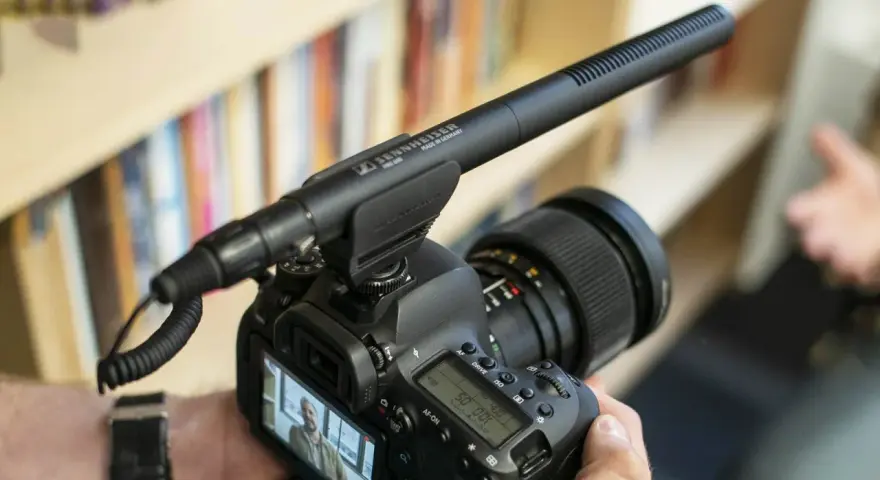 Kamera z mikrofonem kierunkowym Sennheiser MKE 600 na gorącej stopce. Tło to półka z książkami.