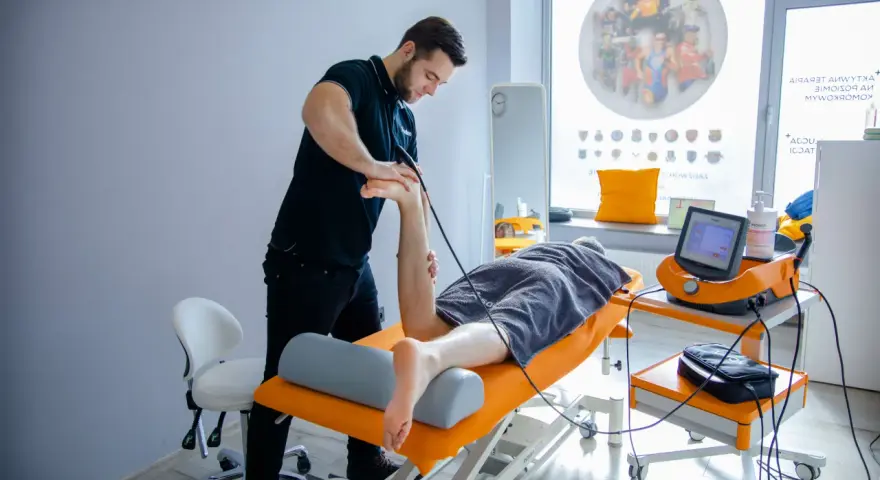Fizjoterapeuta wykonuje zabieg naświetlania kręgosłupa pacjentowi leżącemu na kozetce.