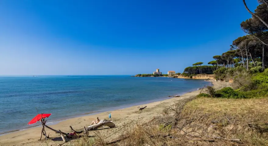 Torre Astura e la sua spiaggia, con un ombrellone rosso e una persona che si rilassa su un tronco.