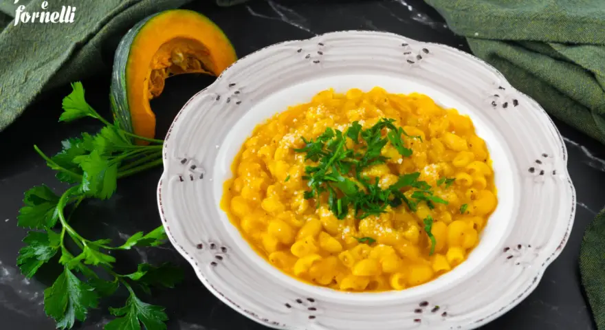 Piatto di pasta e zucca alla napoletana, guarnito con prezzemolo fresco e parmigiano. Accanto, una fetta di zucca e un mazzetto di prezzemolo.
