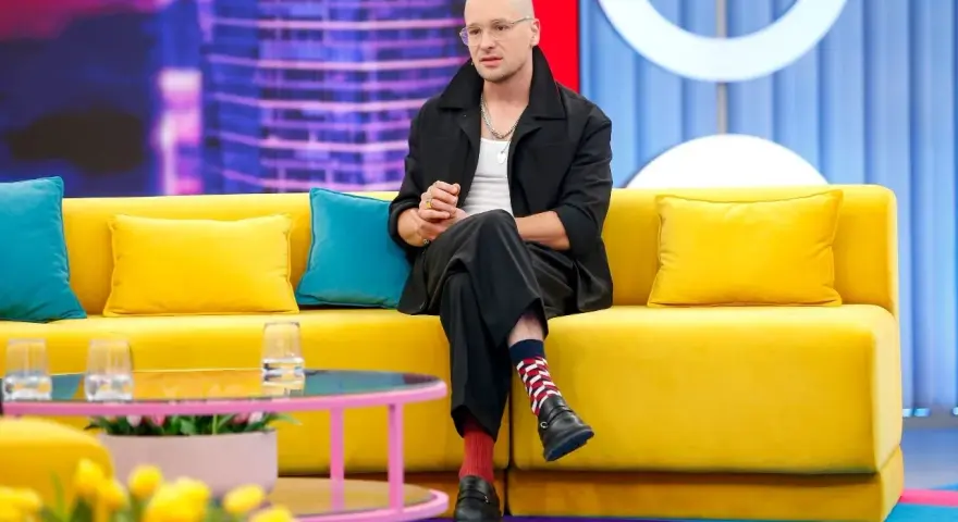 Krzysztof Zalewski w czarnym garniturze siedzi na żółtej kanapie, jakby przygotowywał się do nagrania jednego z jego filmów.