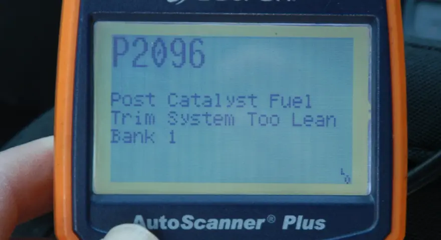 An orange and blue Actron AutoScanner Plus displays error code P2096: Post Catalyst Fuel Trim System Too Lean Bank 1.