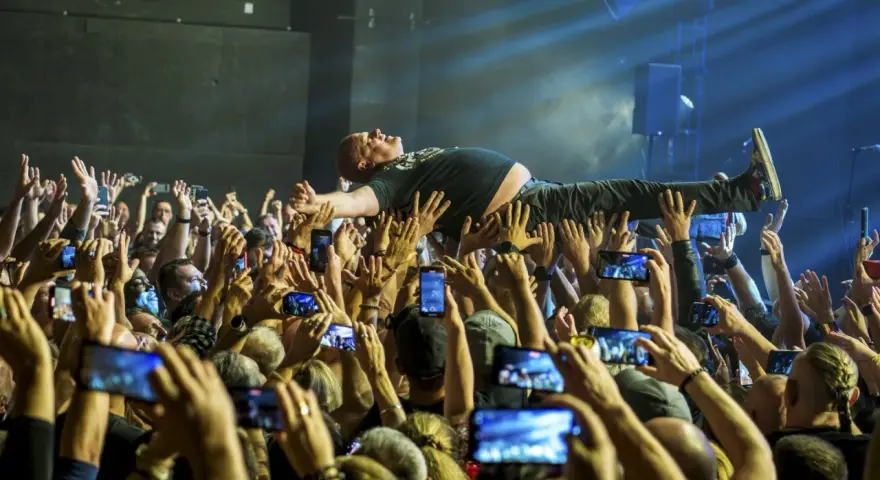 Kult w Arahji: wokalista zespołu niesiony przez tłum, fani nagrywają koncert telefonami.