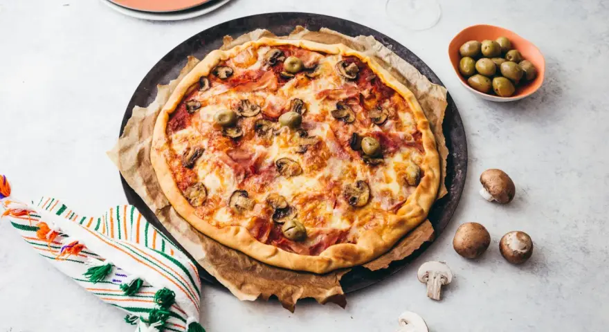 Une délicieuse pizza reine, garnie de jambon, champignons et olives, prête à être dégustée.