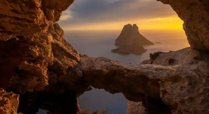 Widok z jaskini na skalistą wysepkę Es Vedrà, jedną z najpiękniejszych wysp Balearów, o zachodzie słońca.
