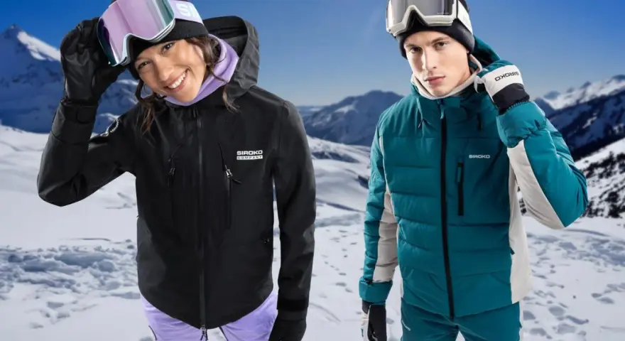 Coppia con abbigliamento da sci, giacche hardshell e maschere da neve, su sfondo montuoso innevato.