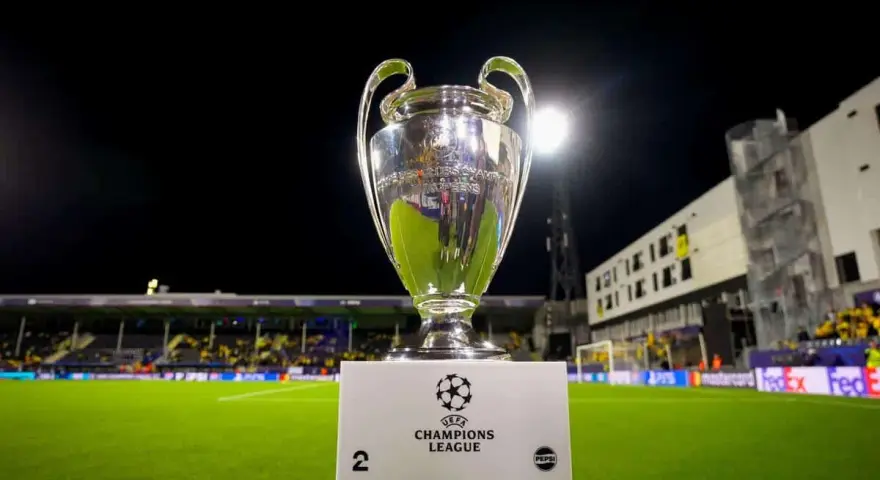 Puchar Ligi Mistrzów na tle stadionu. Ile drużyn awansuje do ligi mistrzów? To pytanie zadają sobie kibice.