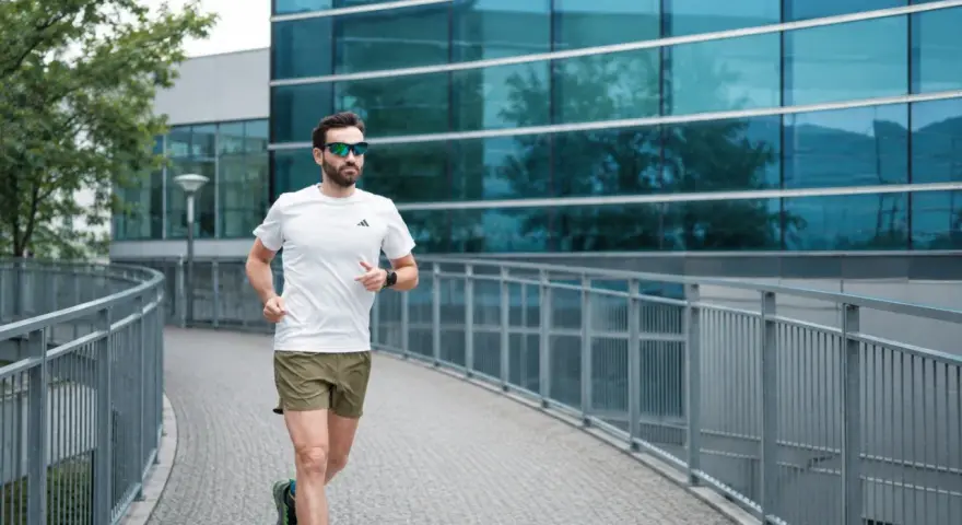 Uomo con barba corre su un ponte moderno, mostrando cos'è il running: libertà e benessere tra architettura e natura.