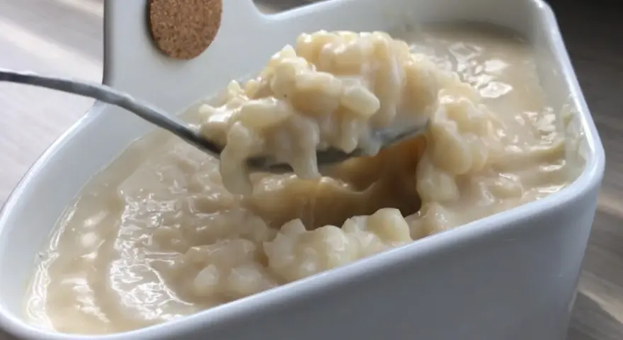 Cuillère prélevant une portion crémeuse de riz au lait dans un bol blanc.