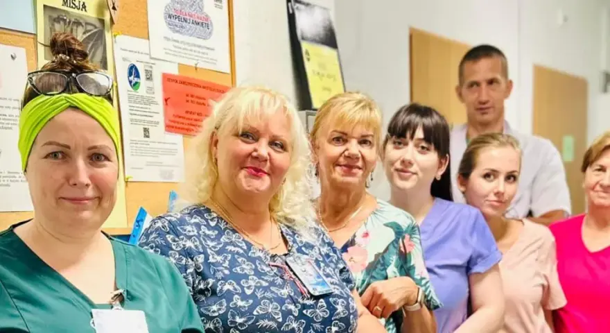 Grupa uśmiechniętych pracowników medycznych w szpitalu, na tle tablicy ogłoszeń.