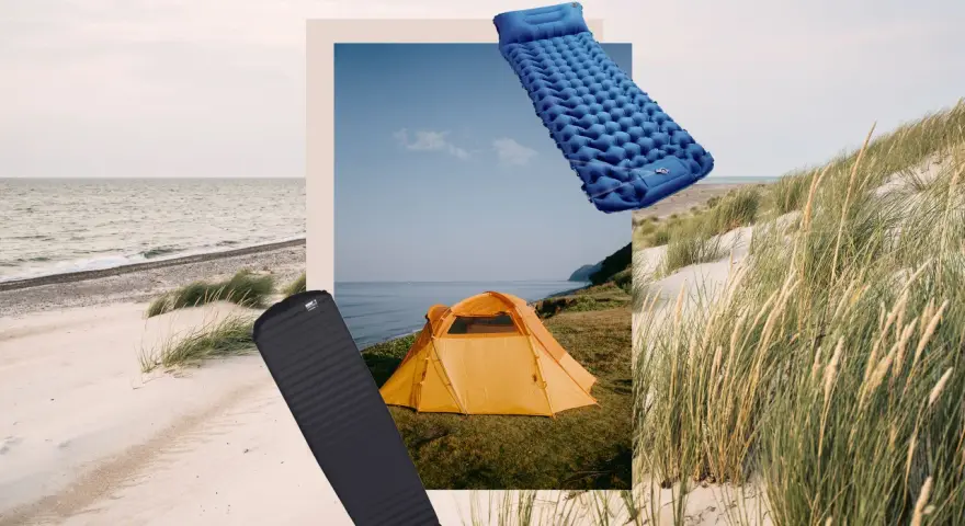 Zwei Isomatten, eine blaue aufblasbare und eine schwarze Schaumstoffmatte, liegen neben einem orangefarbenen Zelt am Strand.