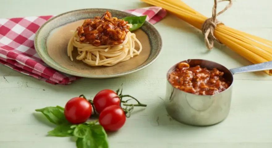 Pyszny sos do spaghetti z mięsem mielonym, podany na talerzu z makaronem, obok świeżych pomidorków i bazylii.