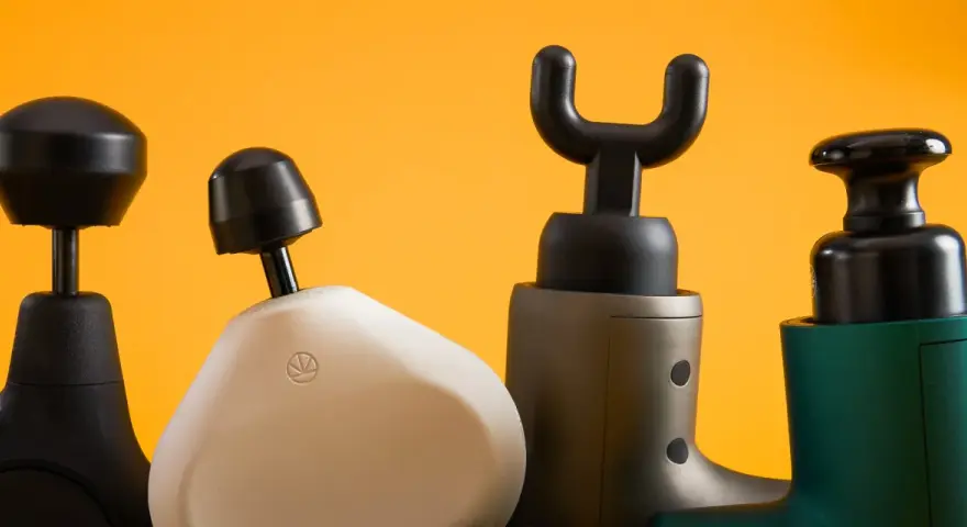Four percussion massagers with different attachments are lined up against a bright orange background.