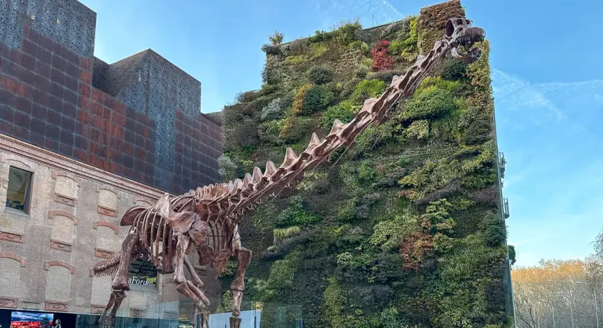 Szkielet dinozaura przed zieloną ścianą budynku. Madryt nietypowe atrakcje, które zaskakują.