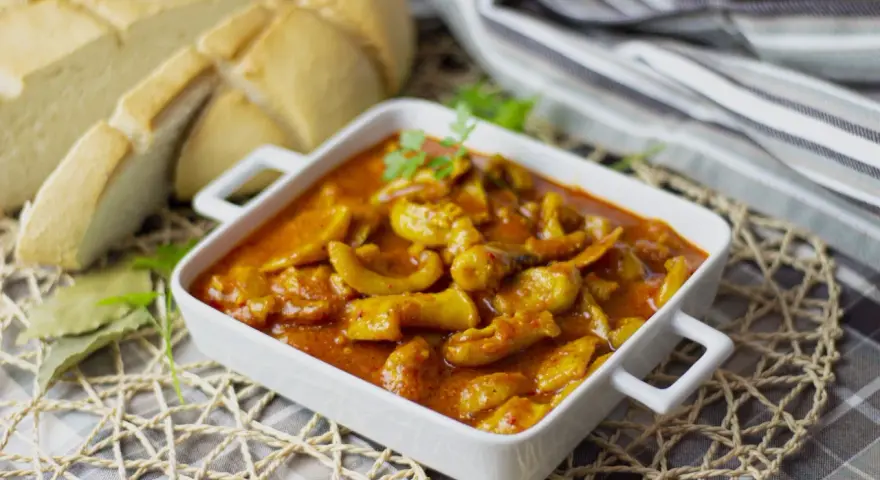 Delicioso plato de sepia en salsa, servido en cazuela blanca, acompañado de pan rústico y hojas de laurel.