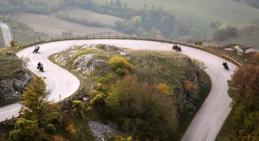 Motociclisti sfrecciano sulle curve delle Gole del Furlo, immersi in un paesaggio autunnale.