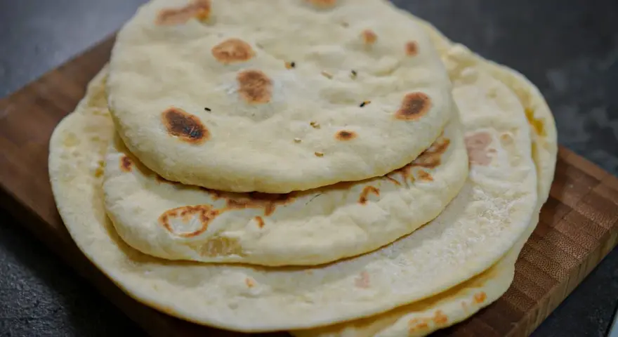 Pile de pains arabes moelleux, légèrement dorés par la cuisson, sur une planche en bois. Parfait pour accompagner un repas.