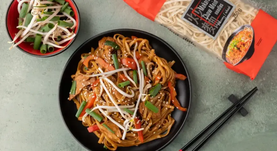Pyszny makaron sojowy z kurczakiem jak od chińczyka, z kiełkami fasoli mung i szczypiorkiem. Obok opakowanie makaronu chow mein.
