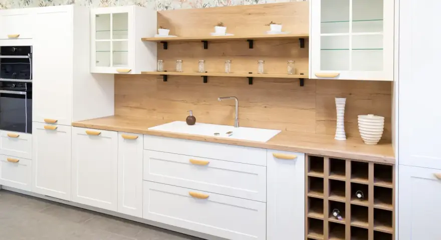 Cocina moderna blanca con encimera de madera, estantes flotantes y botellero. Inspiración para tus ideas de cocinas.