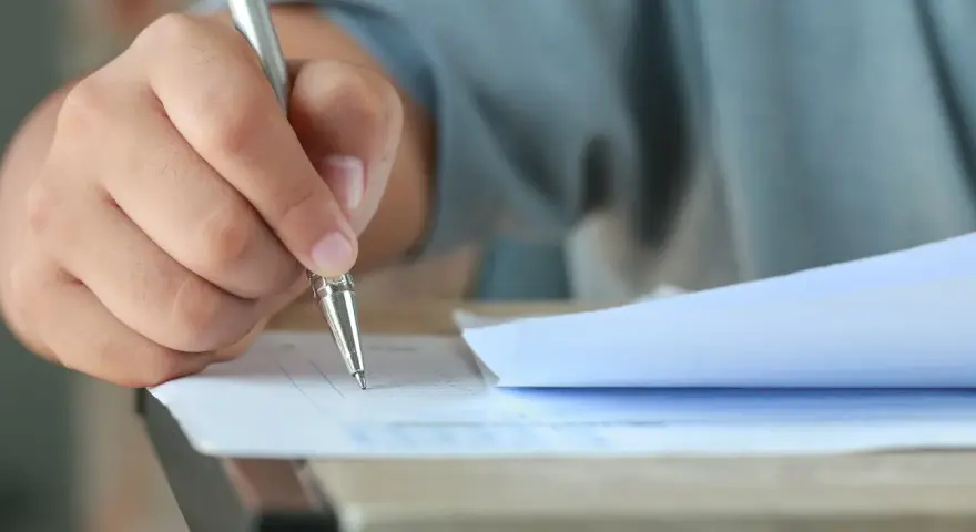 Dłoń trzymająca długopis, która wypełnia test. Czy przed jak również stawiamy przecinek, gdy piszemy.