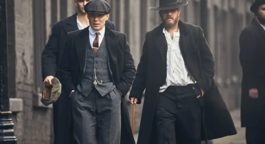Tommy Shelby e altri uomini in abiti eleganti camminano per strada.